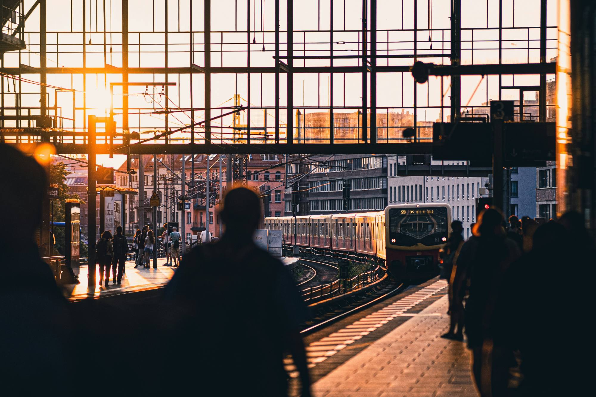 A city rail platform at dusk, commuters in silhouette