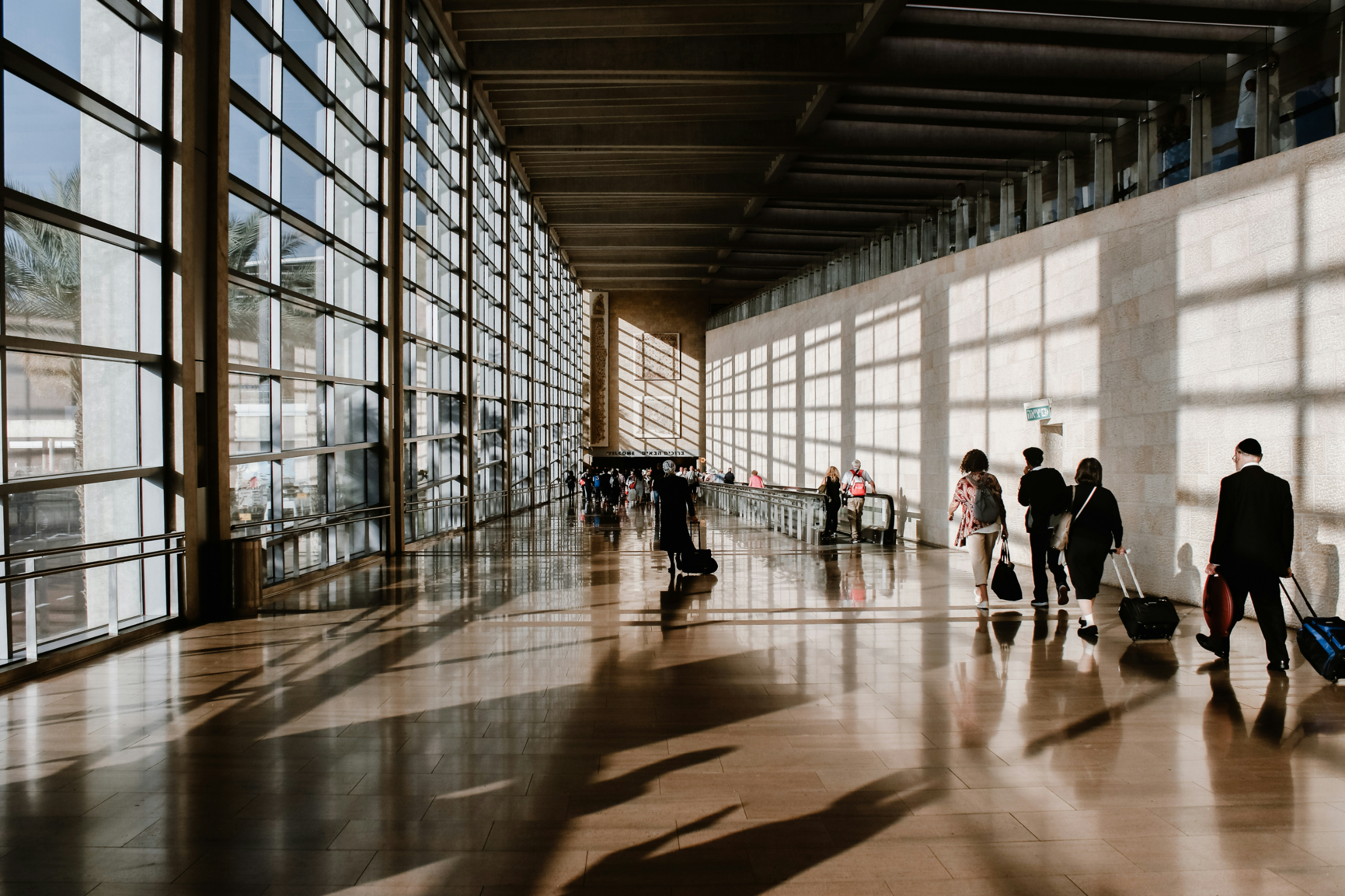 A long glazed corridor, travellers walking through light