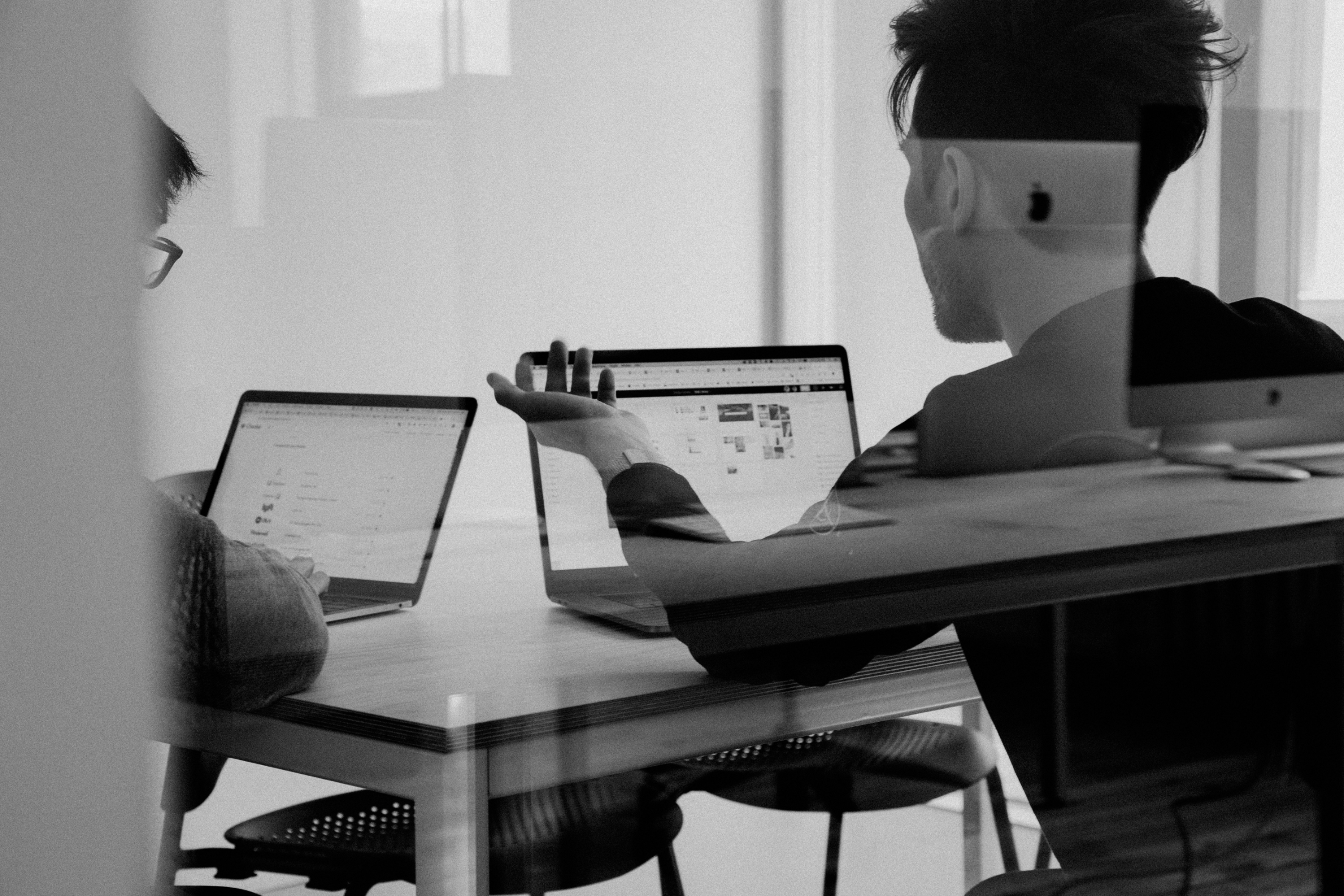 Two people in conversation across a table, seen through glass